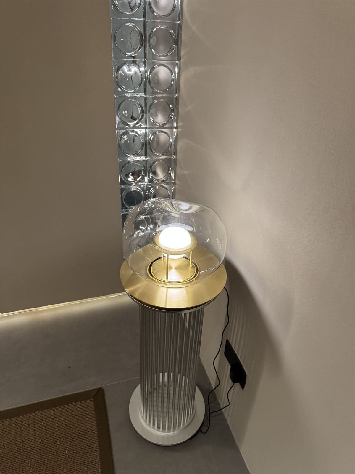 A modern GUOCIO floor lamp with a clear glass dome and brass accents stands next to a decorative wall panel with circular glass elements