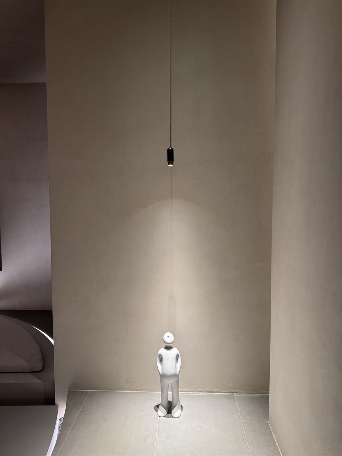 A minimalist black cylindrical GUOCIO pendant illuminates a white abstract human figure sculpture in a neutral-toned room