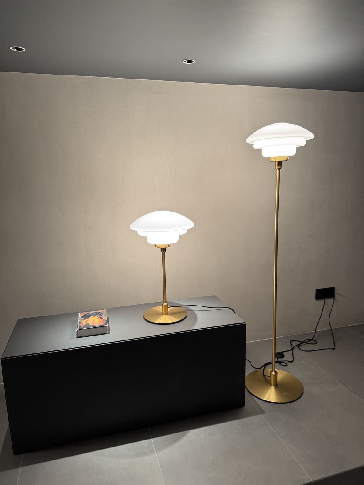 A GUOCIO Venus table lamp on a black plinth and a taller Venus floor lamp, both with tiered white shades and brass stems