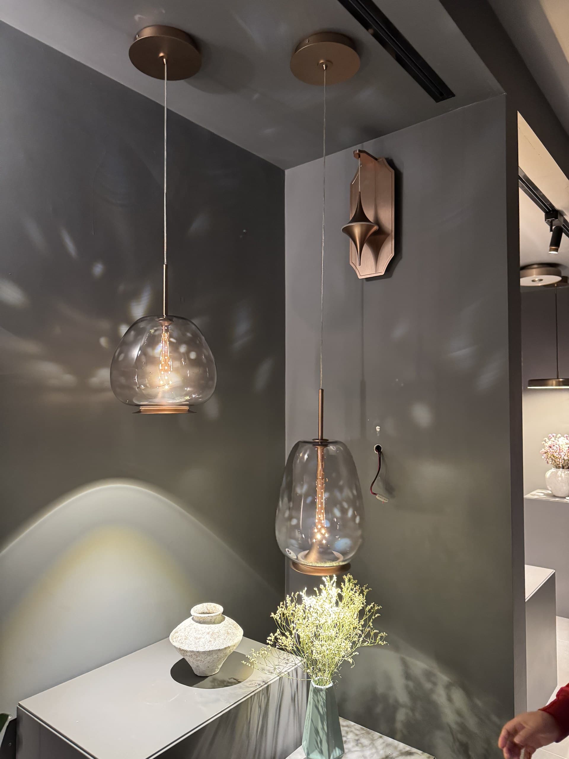 Two glass pendant lights with warm glow illuminate a corner display with decorative objects.